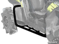 A close-up shows Polaris RZR XP 900 Heavy Duty Rock Sliding Nerf Bars in black metal attached to an off-road vehicle with large, rugged tires. The grayscale image highlights the nerf bars in full color, with the SuperATV logo in the corner.