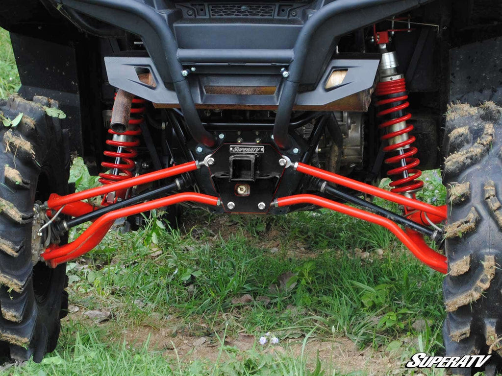 Close-up of a Polaris RZR XP 900 Rear Receiver Hitch installed, featuring rugged rear suspension, bright red shock absorbers, mud-treaded off-road tires on green grass. The SuperATV logo is in the bottom right corner.