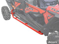 A red Polaris RZR XP 4 Turbo with metal Rock Sliding Nerf Bars is shown. The tubular nerf bars protect the lower side panels between the wheels, and the SuperATV logo appears at the bottom right.