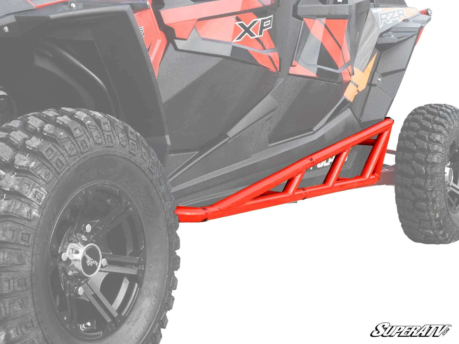 A close-up of Polaris RZR 4 900 Nerf Bars, red metal bars mounted on a black and red off-road vehicle with large knobby tires. The SuperATV logo appears at the lower right, and the faded background highlights the nerf bars.
