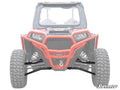 A front view of a red off-road vehicle showcases its large rugged tires, front winch, and reinforced Polaris RZR XP Turbo High-Clearance A-Arms. The suspension stands out while the rest is faded. SuperATV logo appears in the lower-right corner.