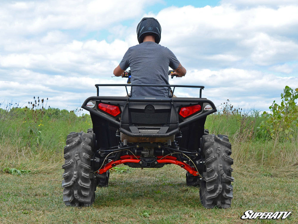 A person in a helmet and gray shirt sits on a black ATV with large rugged tires, red suspension, and rear cargo rack, featuring the Polaris Sportsman XP 4 Portal Gear Lift, in an open grassy field under a partly cloudy sky.