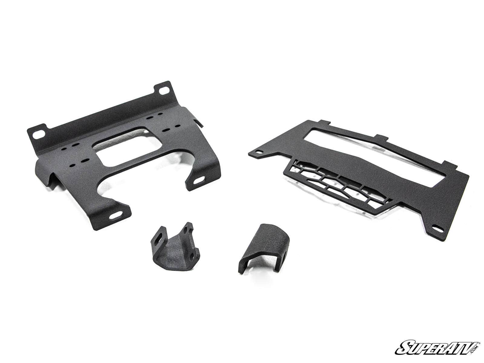 Four black metal brackets of varying shapes and sizes, part of the Polaris General Winch Mounting Plate kit, are displayed on a white background with mounting holes visible and the SuperATV logo in the bottom right corner.