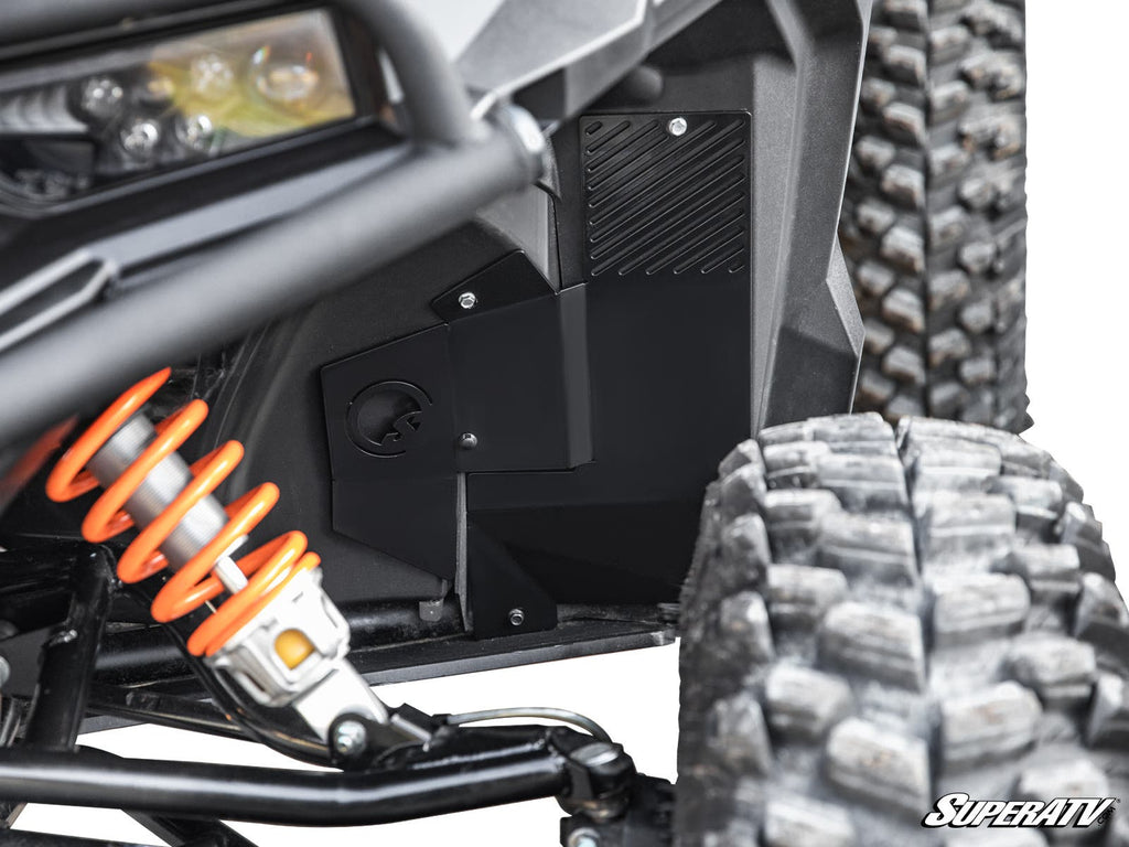 Close-up of a Polaris General XP 1000 Inner Fender Guard installed, highlighting a large orange coil-over shock, rugged tire tread, and black textured guard near the wheel well. The SuperATV logo is visible in the lower right corner.