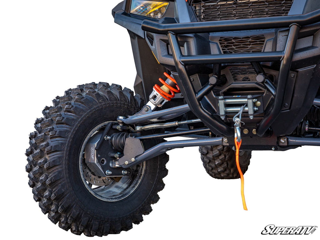 Close-up of the front left wheel and suspension on a Polaris General XP 1000 with 4 Portal Gear Lift; features large rugged tires, orange shock absorber, winch with orange rope, black frame, mesh grille, and SuperATV logo in the bottom right corner.