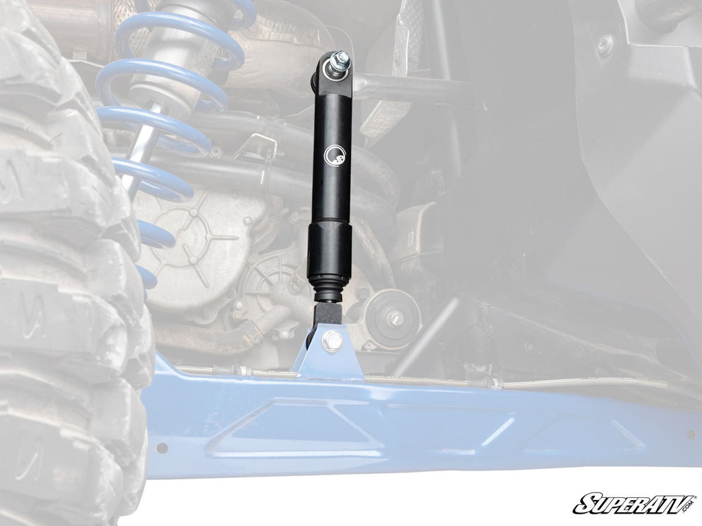 Close-up of a Polaris RZR PRO XP Sway Bar Shock in a blue suspension system. The black shock absorber and coil spring are highlighted with a faded background. Tire, chassis, and SuperATV logo visible.