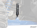 Close-up of a Polaris RZR PRO XP Sway Bar Shock in a blue suspension system. The black shock absorber and coil spring are highlighted with a faded background. Tire, chassis, and SuperATV logo visible.