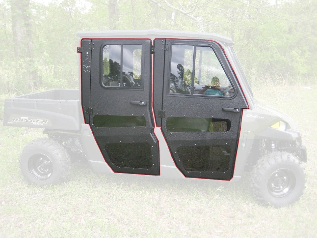 A Polaris Ranger Mid Size 570 Crew (2014-2021) with Full Steel Doors by Armor Tech is shown in profile. The black, angular doors feature large windows and red outlines. Background elements like grass and trees appear faded.