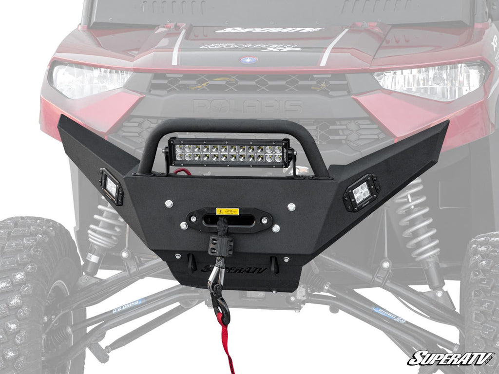 A close-up shows the Polaris Ranger XP 1000 Winch-Ready Bumper with Bull Bar in black, featuring a mounted LED light bar and winch on a red Polaris off-road vehicle. The angular design, sturdy build, and SuperATV logo are clearly visible.