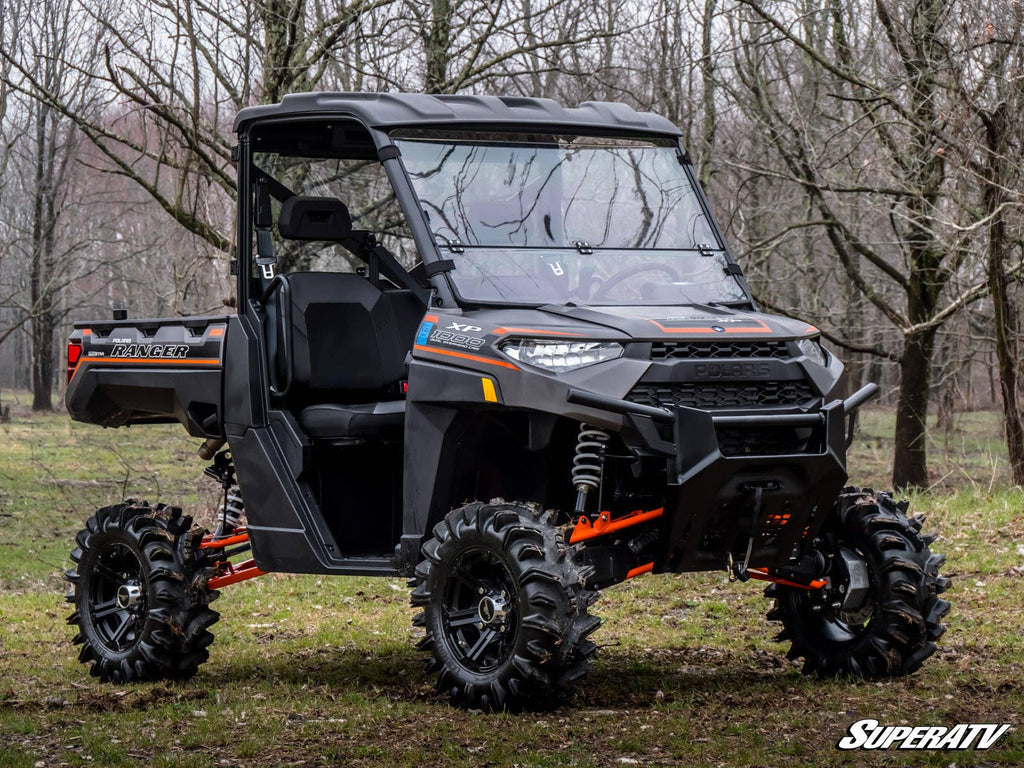 A black Polaris Ranger XP 900 with lifted suspension, rugged tires, and orange accents is parked on grass in a forest. It features a Flip Down Windshield and has the SuperATV logo visible in the bottom right corner.