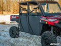 A Polaris Ranger 1000 with black Aluminum Doors by SuperATV, rugged tires, and red body is parked on a snowy grassy area near leafless trees under a clear sky.