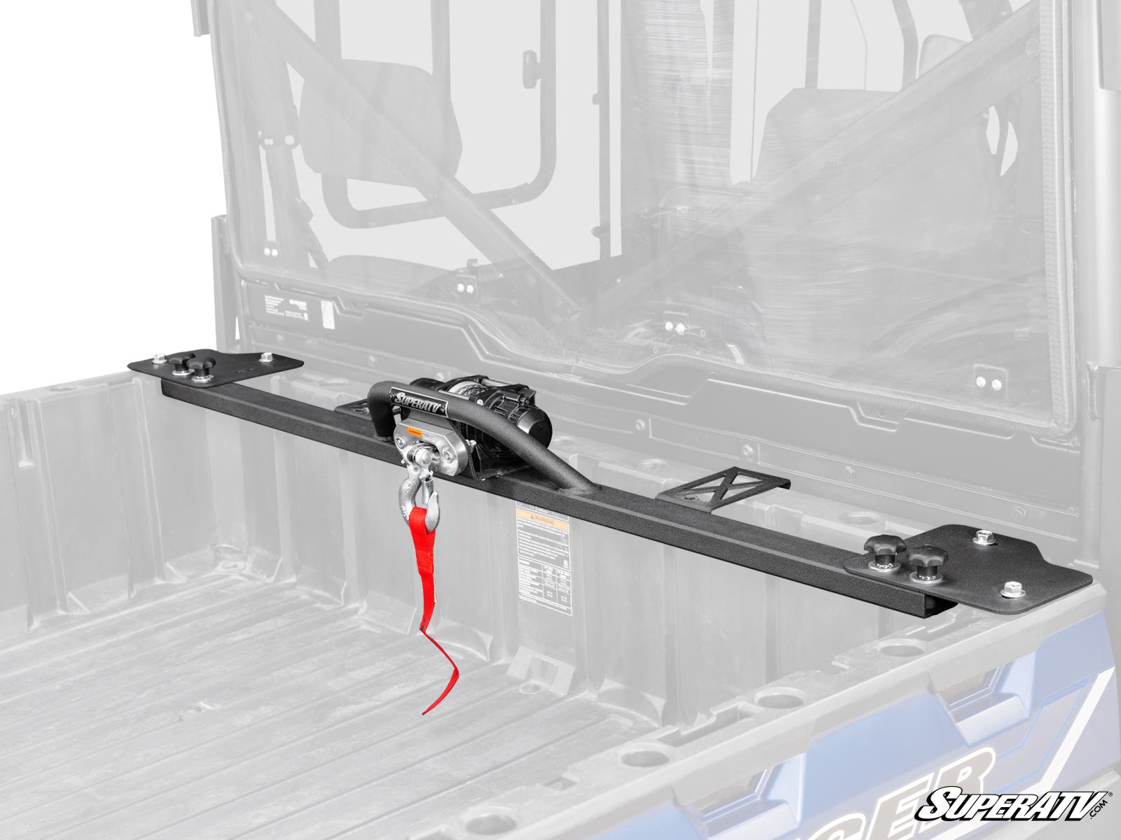 A close-up of the Polaris Ranger 570 Bed Winch with a red strap is mounted in the cargo bed of a blue utility vehicle. The vehicles bed and cab interior are visible, with the SuperATV logo at bottom right and a faded background for emphasis.