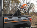 A Polaris Ranger Chainsaw Mount secures a chainsaw in the cargo bed of a Polaris Ranger ProStar. Leafless trees and grass in the background suggest an outdoor setting in late fall or early spring.