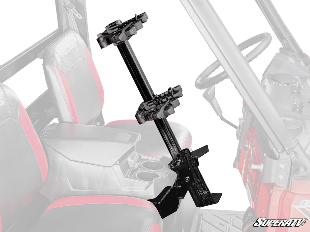 A Polaris Ranger XP 900 Floor-Mounted Gun Holder is installed between the front seats of a red and black off-road vehicle, holding items upright with padded clamps at both ends. The mount attaches to the floor and features the SuperATV logo in the corner.