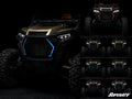 A rugged off-road vehicle with a custom Polaris RZR Fang Lights grill is shown. The main image features blue LEDs, while six smaller images show the grill in red, purple, orange, green, pink, and white LEDs. SuperATV logo appears in the corner on a dark b