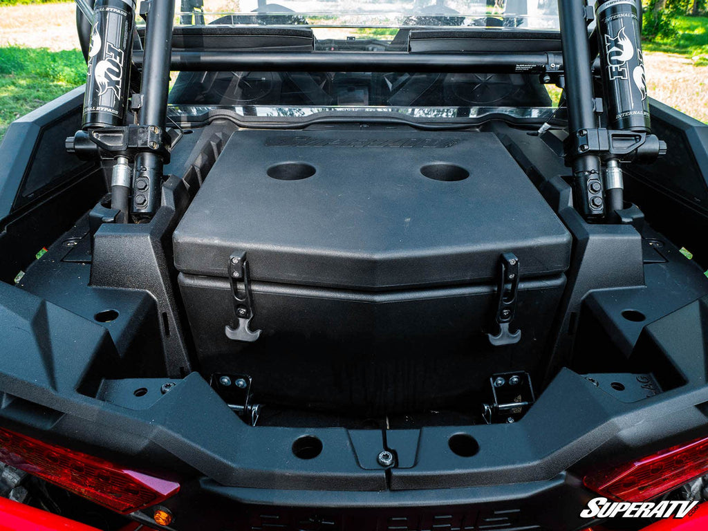 A close-up of the rear cargo area shows a Polaris RZR XP Turbo Cooler / Cargo Box—large, black, and rectangular—secured with latches. Heavy-duty gas struts and roll cage bars are visible, with the SuperATV logo in the bottom right corner.