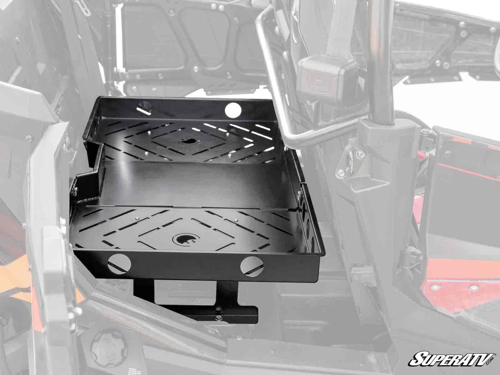 A Polaris RZR XP 4 Turbo S Rear Seat Cargo Rack with black metal slotted surfaces and round holes is mounted next to the drivers seat inside the cab; part of the vehicle interior is visible in the background.