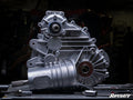 A close-up of a Polaris RZR Trail 900 Complete Heavy-Duty Transmission sits on a workbench with tools. Intricate gears and bolts are visible, set against a dark, blurred background with the SuperATV logo in the corner.