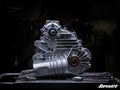 The Polaris General 1000 Complete Heavy-Duty Transmission gleams on a dark workbench, surrounded by wrenches and a ratchet. A dim, blurred background highlights the machinery, with the SuperATV logo in the lower right corner.