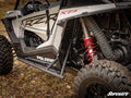 Close-up of Polaris RZR XP Turbo Tree Kickers installed on a Polaris RZR XP, showing rugged tires, red coil spring suspension, visible Polaris and RZR logos, with autumn leaves scattered on the ground.