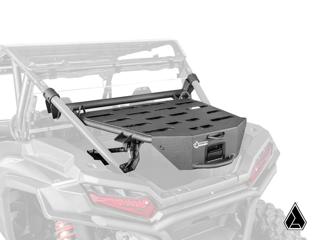 The Assault Industries Polaris RZR XP Adventure Rack, a sturdy black metal cargo rack with a grated platform, handle, slotted surface, and robust tubular supports, is mounted on the rear bed of an off-road vehicle shown in grayscale.