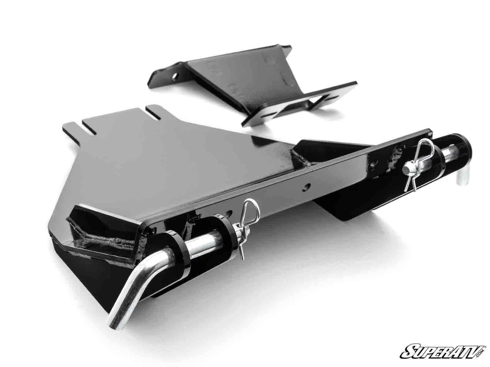 The Polaris RZR 570 Plow Pro Snow Plow Mount is a black metal bracket with a slanted, angular design and two cylindrical pins secured by cotter pins. A smaller bracket sits above, with a white background and the SuperATV logo in the bottom right corner.