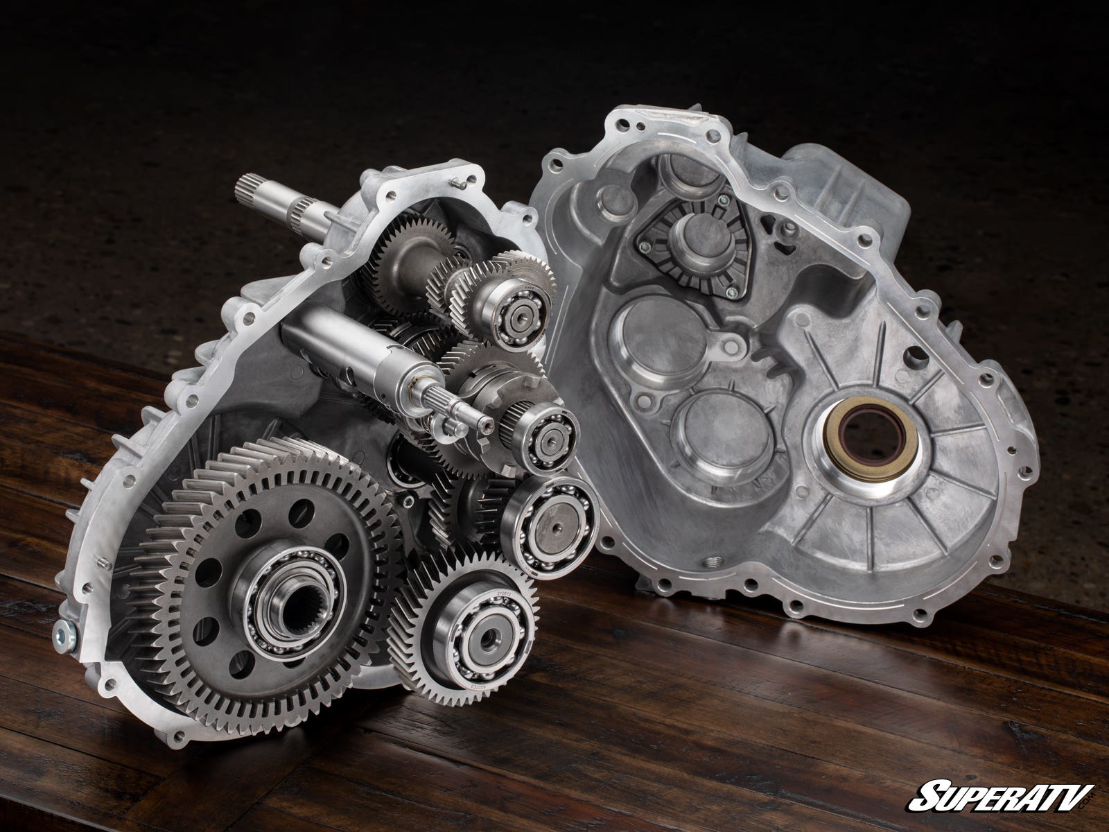 A Polaris Ranger XP 900 Complete Geared-Reverse Transmission sits open on a wooden surface, displaying its intricate gears, shafts, and bearings. All internal components are visible, with the SuperATV logo in the lower right corner.