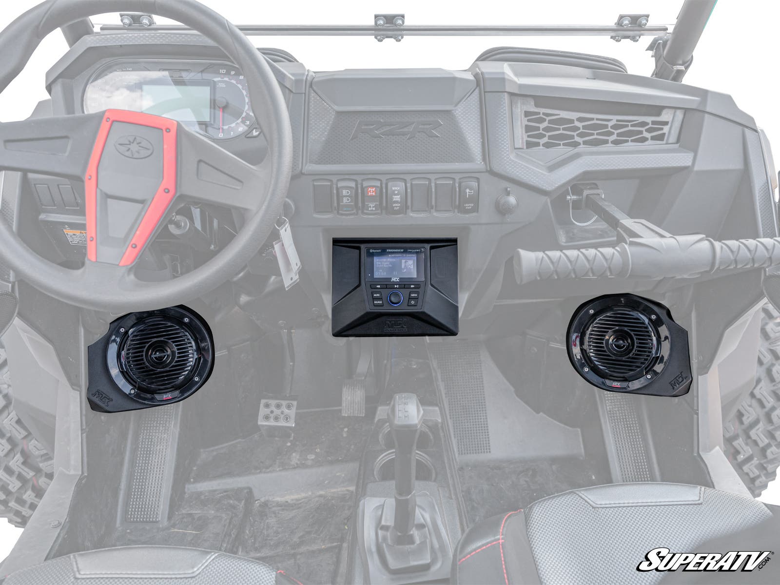 Interior view of a Polaris RZR with the MTX Polaris RZR THUNDER Sound System, showing the dashboard, steering wheel, center console, two black speakers by the footwells, control switches, and the SuperATV logo in the bottom right corner.