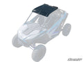 A Polaris RZR PRO XP Tinted Roof is installed on a white and blue off-road UTV. The semi-transparent black roof, secured by corner bolts, stands out as the main feature in the mostly faded image.