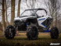 A white and blue Polaris RZR featuring the Polaris RZR PRO XP 6 Portal Gear Lift sits on grassy terrain among bare trees under an overcast sky, with the SuperATV logo visible in the bottom right corner.