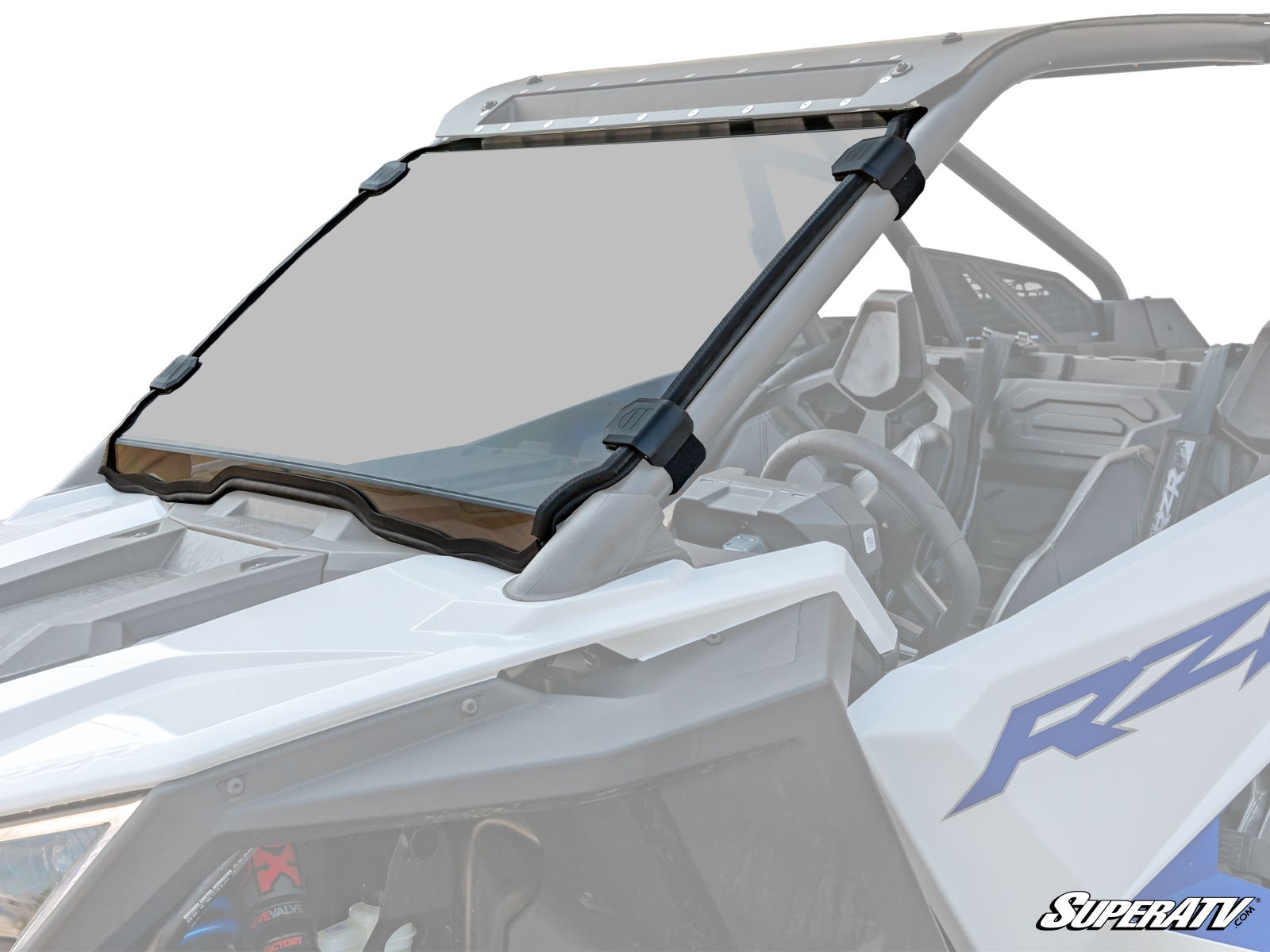 A Polaris RZR PRO XP Scratch Resistant Full Windshield with black clamps is mounted on a white UTV, attaching to the roll cage. The clear windshield has a tinted top strip and reveals the vehicle’s interior and steering wheel.