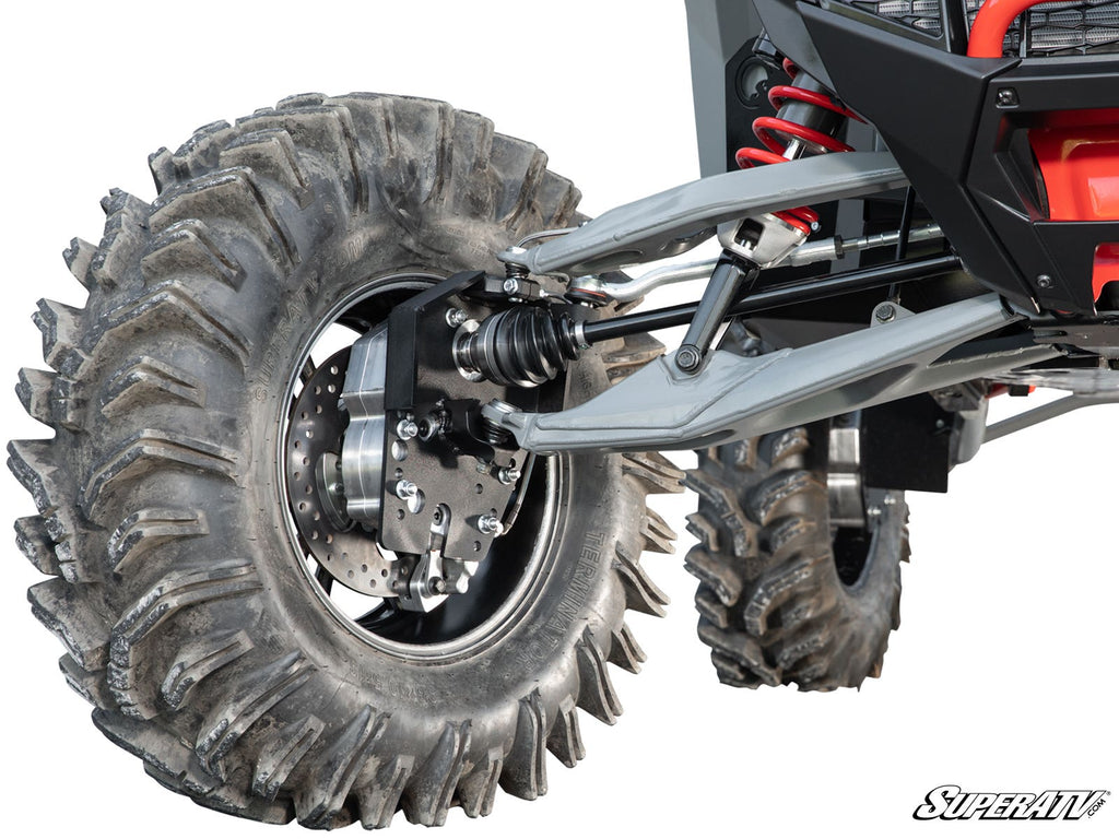 Close-up of a Polaris RZR Turbo R 6 Portal Gear Lift’s rugged suspension system and large, deeply treaded tires, showing shock absorbers, control arms, brake disc, and axle. SuperATV logo is in the bottom right corner.