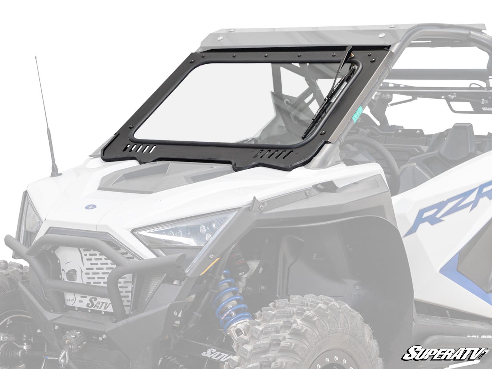 A white off-road vehicle features a Polaris RZR PRO XP Glass Windshield with a black frame, visible bolts, and tilt-out hinge. The vehicle has rugged tires, blue suspension springs, and visible interior seating.