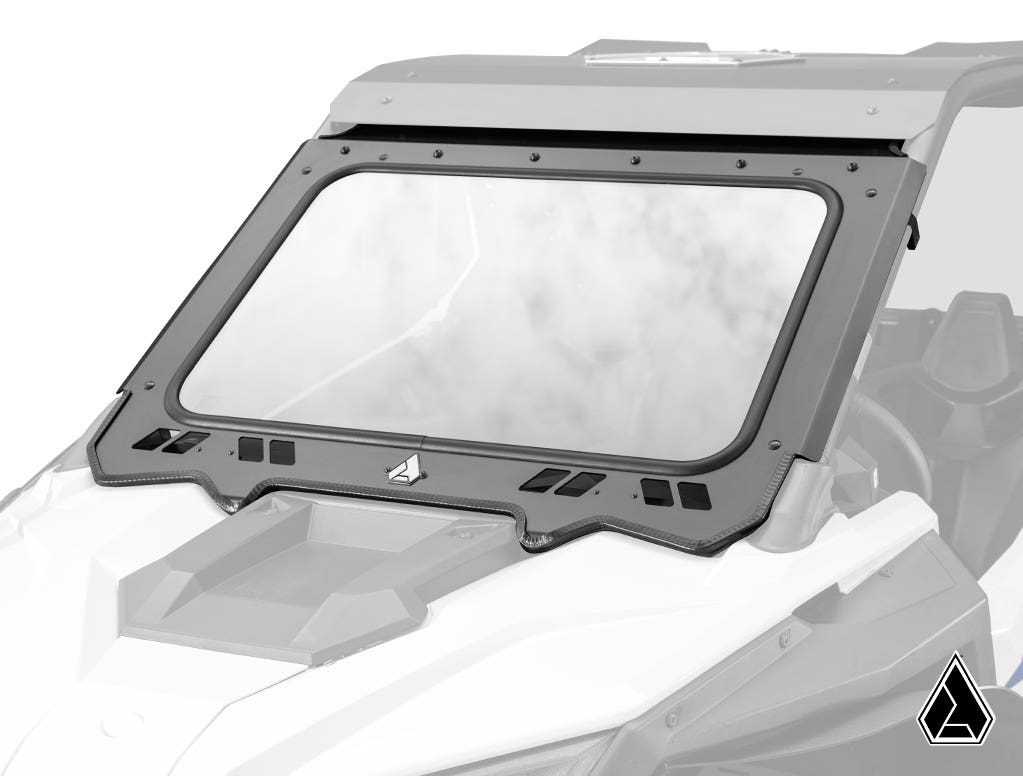 A white off-road vehicle is fitted with an Assault Industries Polaris RZR PRO XP Glass Windshield, featuring a black metal frame, slight tint, ventilation slots, and a center triangle logo; the hood and interior are also visible.