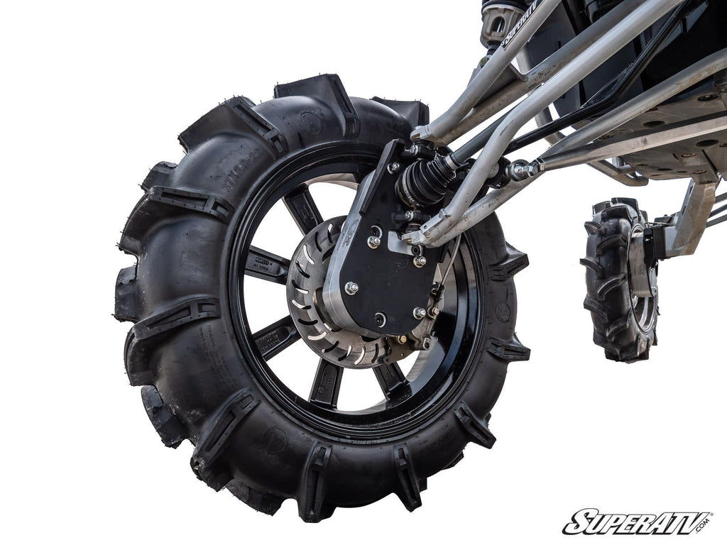 Close-up of a Polaris RZR RS1 8 Portal Gear Lift featuring a large off-road wheel with aggressive tread, black alloy rim, and visible suspension and brake components. A smaller wheel appears in the back. SuperATV logo shown on a white background.