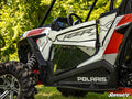 Close-up side view of a white Polaris RZR S4 1000 featuring Clear Lower Doors, rugged black and gray graphics with red accents, and large tires, parked on green grass with leafy trees. SuperATV logo appears in the lower right corner.