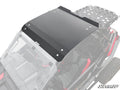 A Polaris RZR Turbo R Aluminum Roof, black and rectangular, is installed on a side-by-side off-road vehicle with red interior accents and a rear metal cargo rack. Secured with bolts, the SuperATV logo appears in the corner, viewed from above at an angle.
