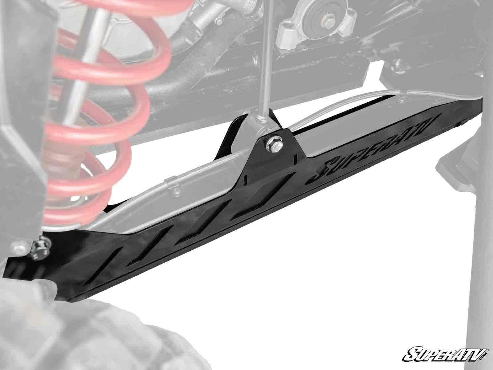 Close-up of Polaris RZR RS1 Trailing Arm Guards by SuperATV, featuring angular black metal design. Mounted on an off-road vehicle with a visible red coil spring and tire, the faded background highlights the guards durability and style.