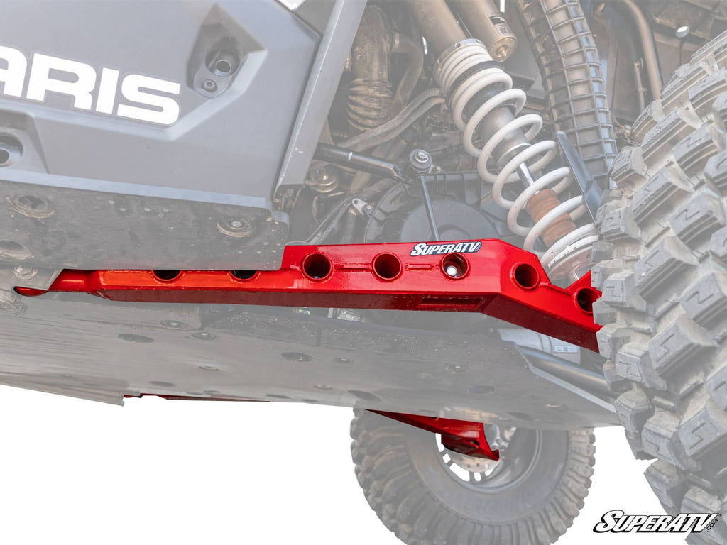 A close-up of Polaris RZR RS1 High Clearance Rear Trailing Arms installed beneath a Polaris off-road vehicle, bolted near the suspension and large tire with visible chassis and mechanical components.