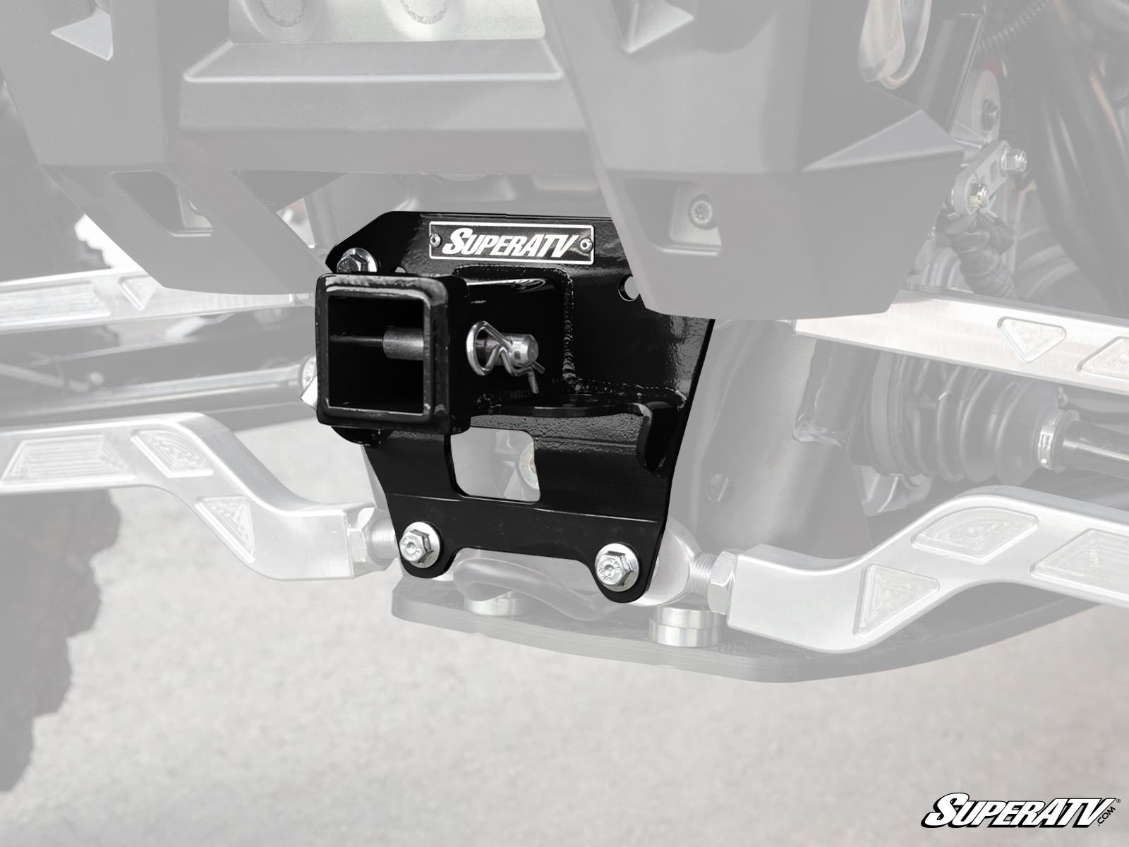 Close-up of a Polaris RZR XP Turbo S Rear Receiver Hitch mounted under an off-road vehicle. The black hitch is bolted in place, with visible suspension arms, metal details, and the SuperATV logo on both the hitch and image corner.