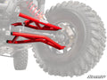Close-up of a Polaris RZR XP 1.5 Forward Offset A-Arms, featuring shiny red control arms and a SuperATV-branded coil spring. The large, knobby tire and exposed axle highlight the vehicle’s durable, high-performance suspension setup.