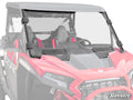 A Polaris RZR XP Vented Windshield with black mounting brackets is installed on a red off-road side-by-side, covering the front seats. The SuperATV logo appears in the bottom right corner.