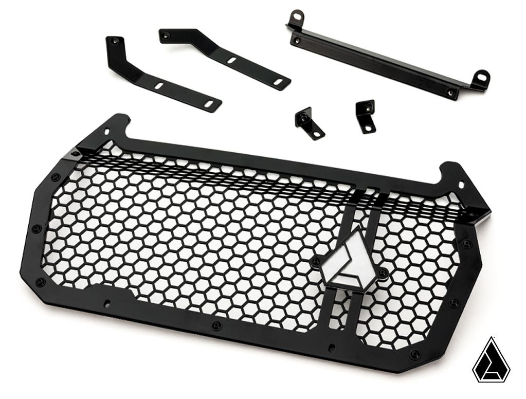 The Assault Industries Polaris RZR XP Hellfire Grille, featuring a black metal honeycomb mesh, triangular logo, and thick border, is displayed with matching mounting brackets and hardware on a white background with a small geometric logo at the bottom rig