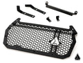 The Assault Industries Polaris RZR XP Hellfire Grille, featuring a black metal honeycomb mesh, triangular logo, and thick border, is displayed with matching mounting brackets and hardware on a white background with a small geometric logo at the bottom rig