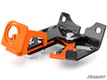 The Polaris RZR Brake Lock is a black and orange metal latch mechanism with visible bolts, a spring, and mounting holes. It features an orange lever and bracket on a black body, straight and curved edges, and the SuperATV logo in the bottom right corner.
