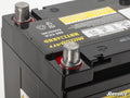 Close-up of a black Polaris RZR Motobatt Battery Replacement, highlighting two metallic terminals, safety and warning labels, part of the brand name, and a visible SuperATV logo in the bottom right corner.