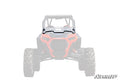 A front view of a red Polaris off-road vehicle is shown with a Polaris RZR Turbo S Half Windshield installed. The background and vehicle are faded to highlight the windshield, with “SuperATV” branded in the lower right corner.