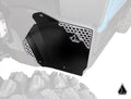 A close-up of Assault Industries Polaris Xpedition Inner Fender Guards highlights a black panel with a honeycomb-patterned metal accent and geometric logo. The vivid panel and nearby textured tire stand out against a desaturated background.