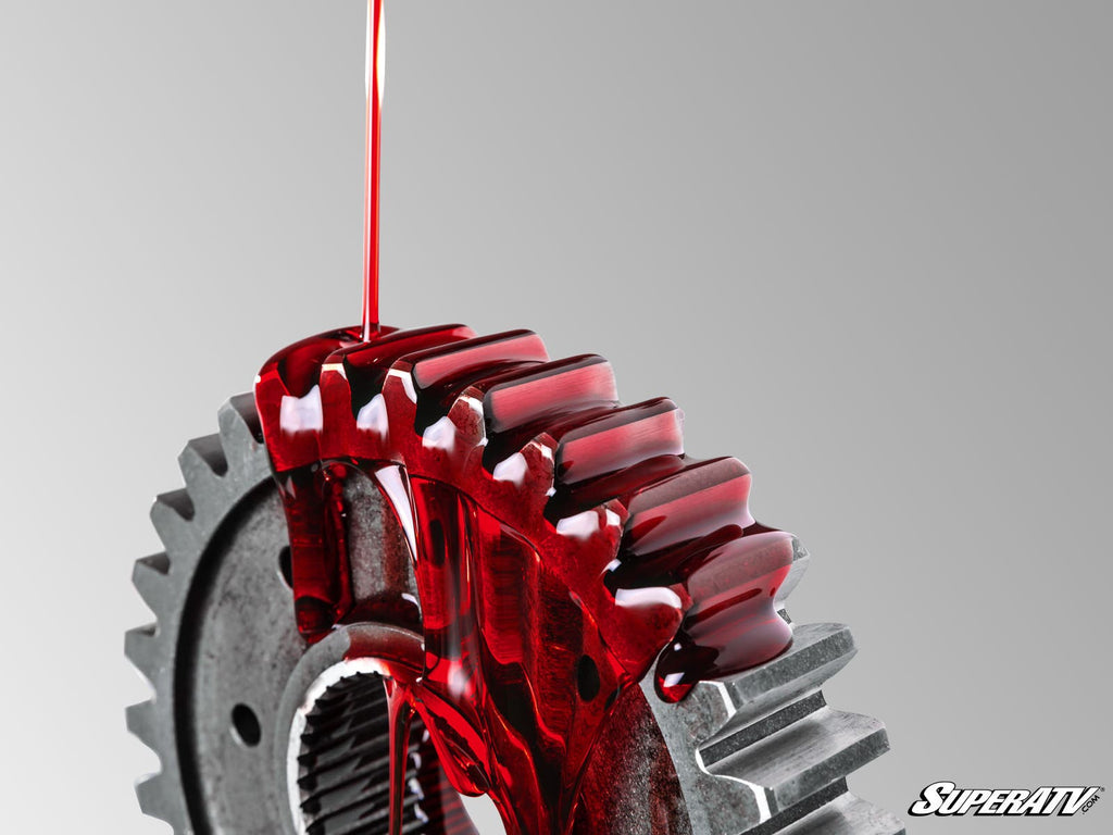 A close-up of red Portal Blood Portal Gear Oil being poured over a metal gear with sharp teeth, partially coated in oil. The background transitions smoothly from light to dark gray, with the “SuperATV” logo in the bottom right corner.