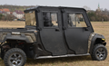 An Arctic Cat Prowler Pro CREW PROTECTOR/Tracker 800 CREW PROTECTOR Cab Kit-equipped black off-road utility vehicle with four doors and rugged tires is parked on dry grass, with textured side panels. Leafless trees and a church spire are visible in the ba